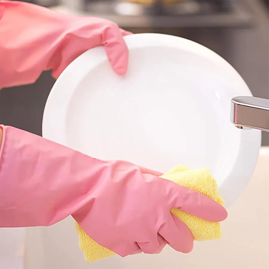 Pink gloved hands rinsing a white plate with a yellow sponge