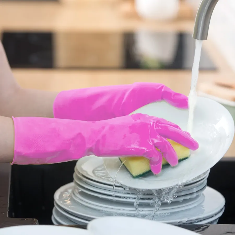 Pink gloved hands washing a stack of white plates under a kitchen faucet