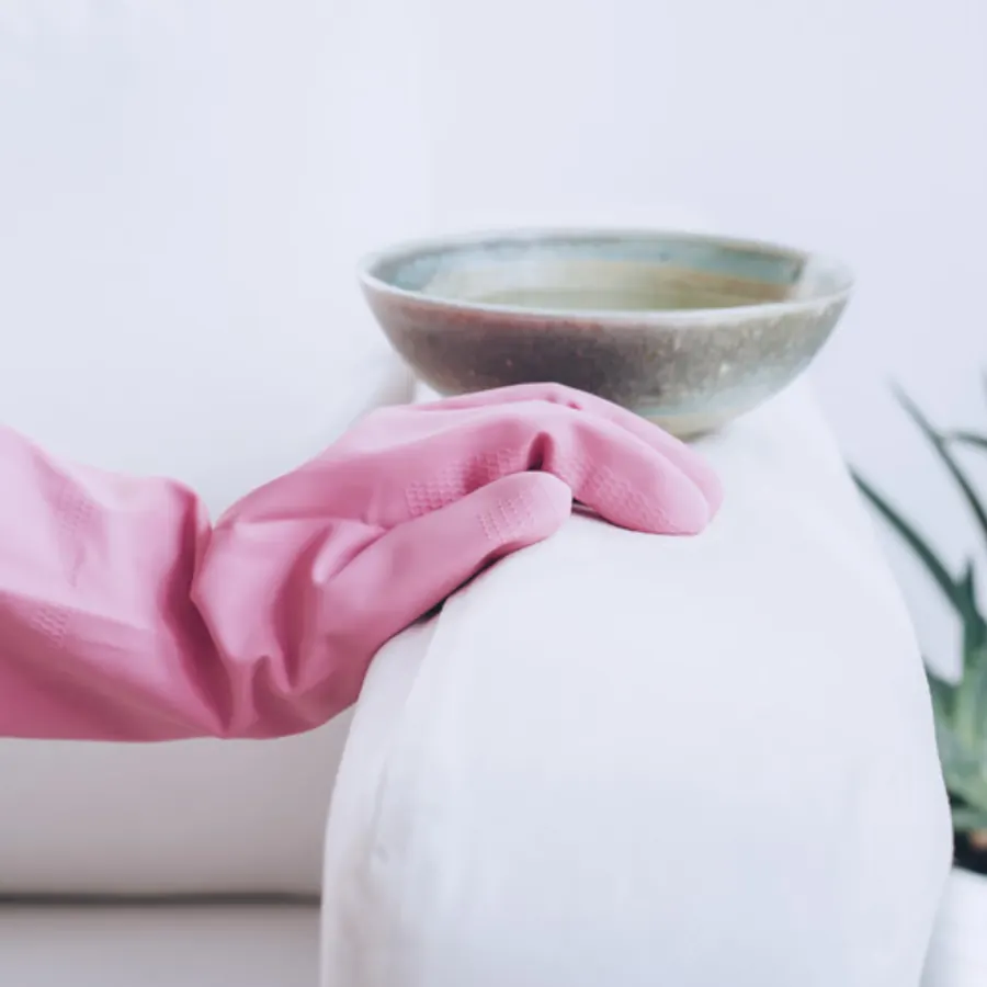 Pink gloved hand resting on a clean white sofa arm next to a ceramic bowl